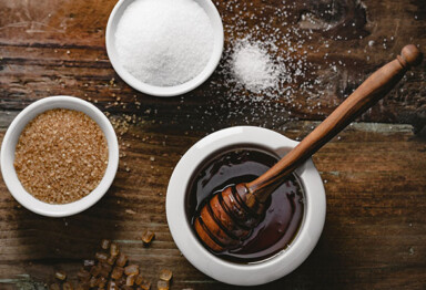 Small pot of honey, brown sugar in a small bowl and white sugar in a small bowl on wood table