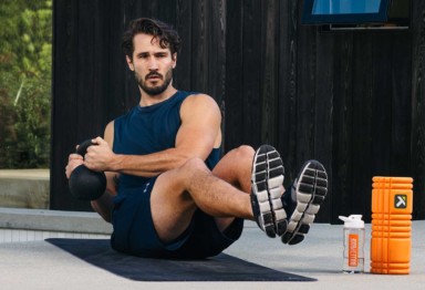 Man on yoga mat performing russian twists with a kettlebell