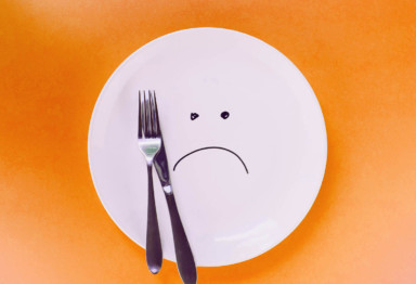 Empty plate and flatware with cartoon sad face