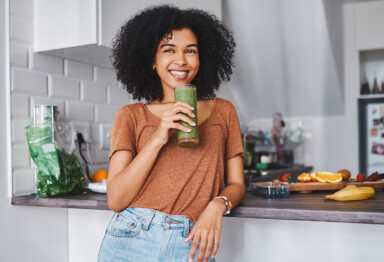 Woman holding green smoothie and smiling in kitchen
