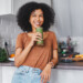 Woman holding green smoothie and smiling in kitchen