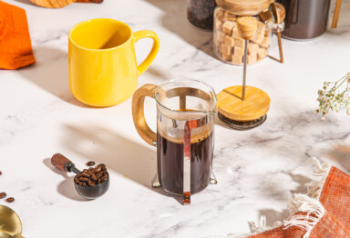 french press of coffee next to yellow mug