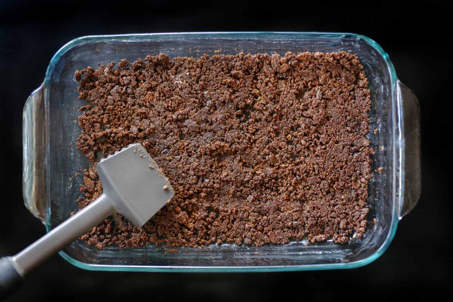smashed cookies in the bottom of a glass baking tray