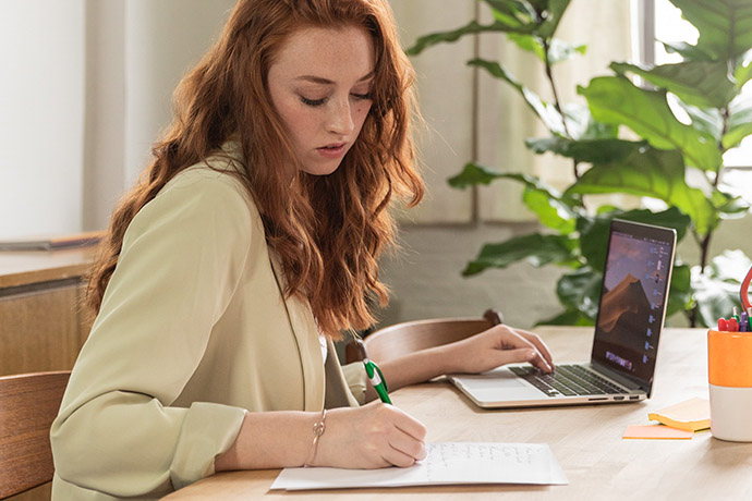 Woman working at desk with laptop and paper and pen