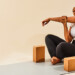 Woman sitting on yoga mat with yoga blocks doing arm stretches and smiling