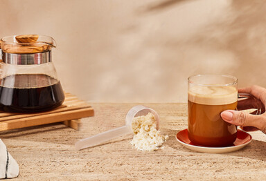 Hand reaching for mug of Bulletproof coffee with scoop of enhanced creamer on kitchen table