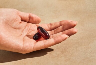 Hand holding 2 gel capsules of fish oil