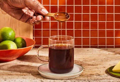 Hand pouring tablespoon of Bulletproof MCT oil into mug of coffee